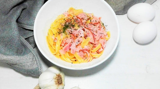 Annoskuva Pasta Carbonarasta. Lautasen vierellä valkosipulia ja kaksi kananmunaa.
