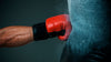 Nyrkkeilijän käsi, jossa on punainen nyrkkeilyhanska, iskeytyy nyrkkeilysäkkiin.