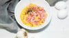 Annoskuva Pasta Carbonarasta. Lautasen vierellä valkosipulia ja kaksi kananmunaa.