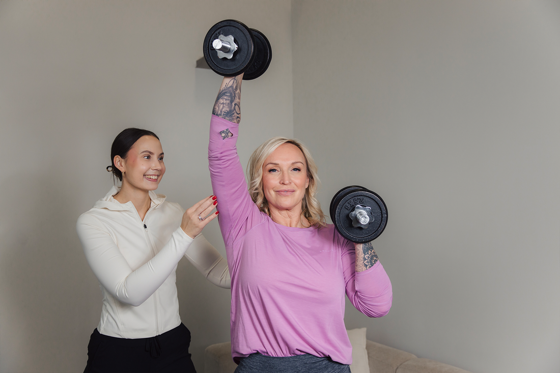 Jutta nostaa käsipainoja, valmentaja vierellä